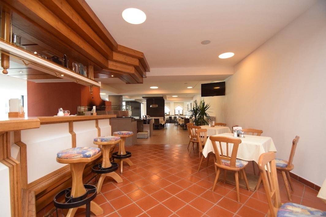 Gemütlicher Restaurantbereich mit Holztheke, Barhockern und traditionellen Esstischen auf Terrakottafliesen.