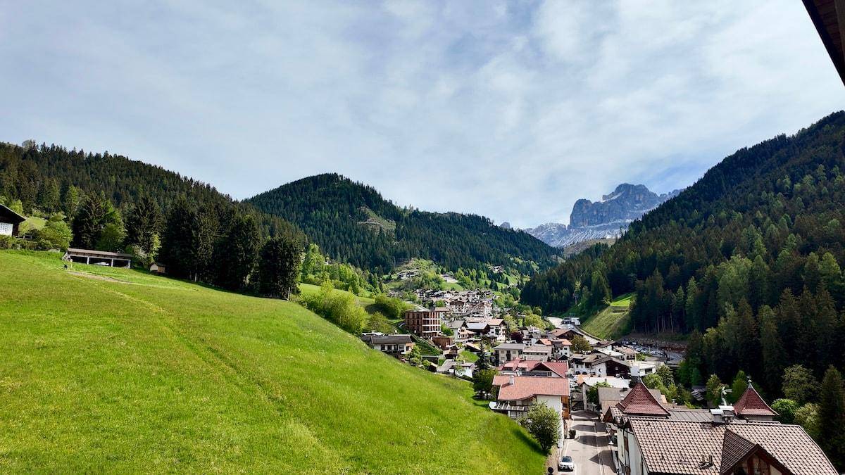 Weitläufiger Blick auf ein malerisches Bergdorf, umgeben von grünen Hügeln und Wäldern.