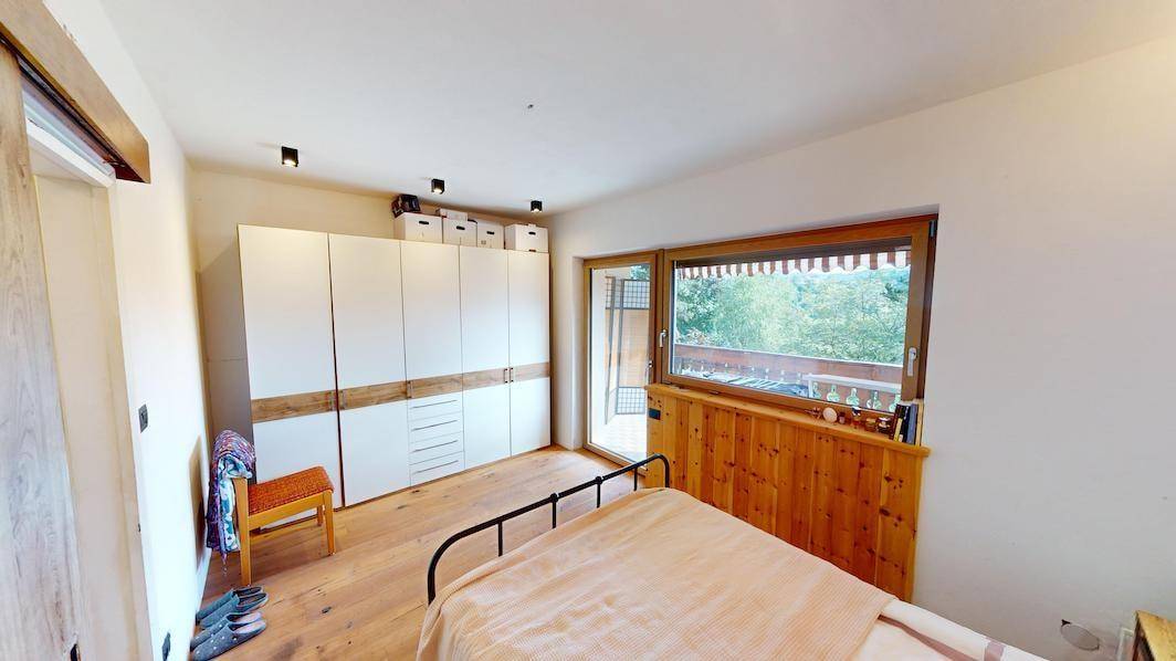 Schlafzimmer mit großem Kleiderschrank, Holzboden und Fenster mit Blick ins Grüne.