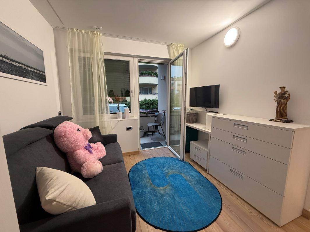 Helles Schlafzimmer mit Schlafsofa, Kommode und Blick auf den Außenbereich.