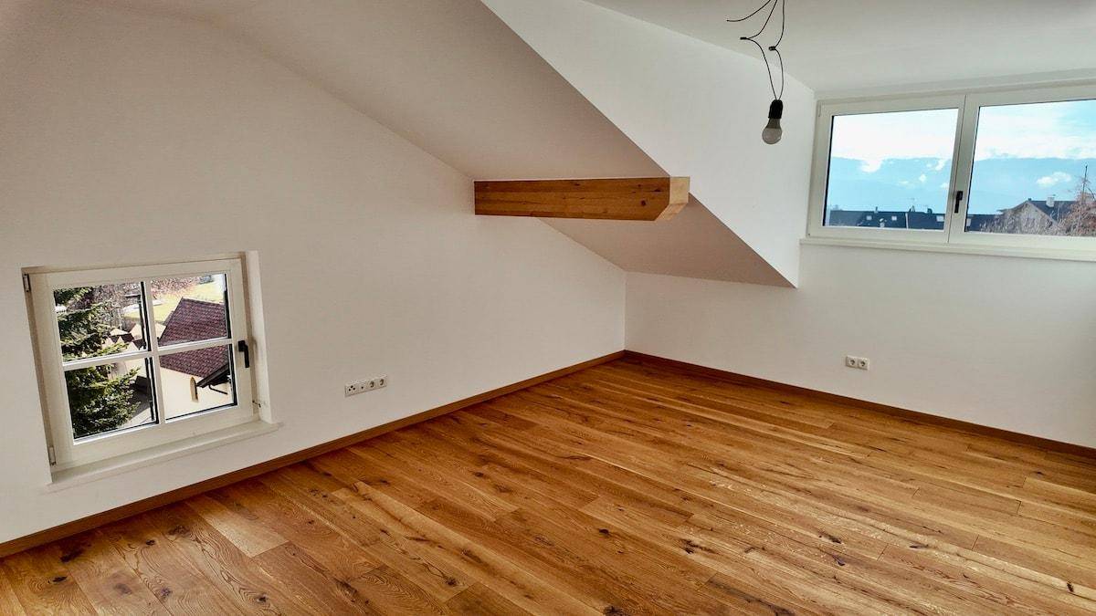 Dachgeschosszimmer mit Holzboden, schrägen Wänden und einem dekorativen Holzbalken.