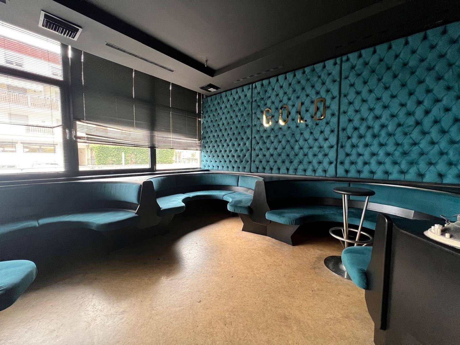 Elegante Lounge mit durchgehenden türkisfarbenen Sitzbänken, dunklen Wänden und großen Fenstern mit Jalousien.