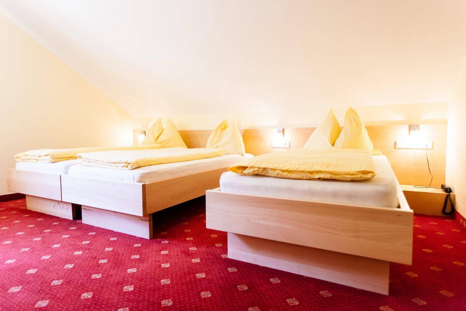 Helles Schlafzimmer mit zwei Einzelbetten, rotem Teppichboden und Dachschräge.
