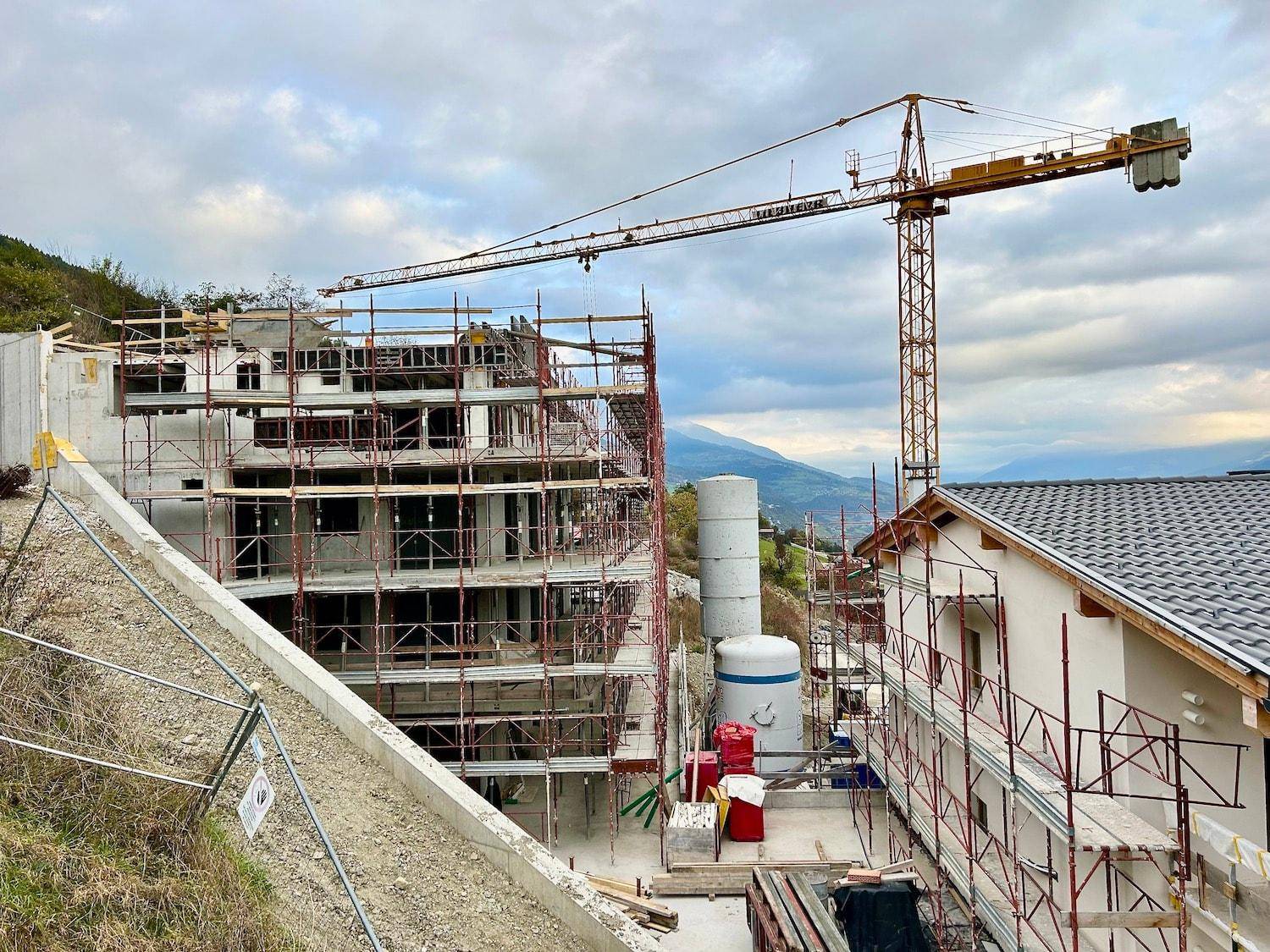 Weitläufige Baustelle mit mehreren im Bau befindlichen Gebäuden und einem großen Kran.