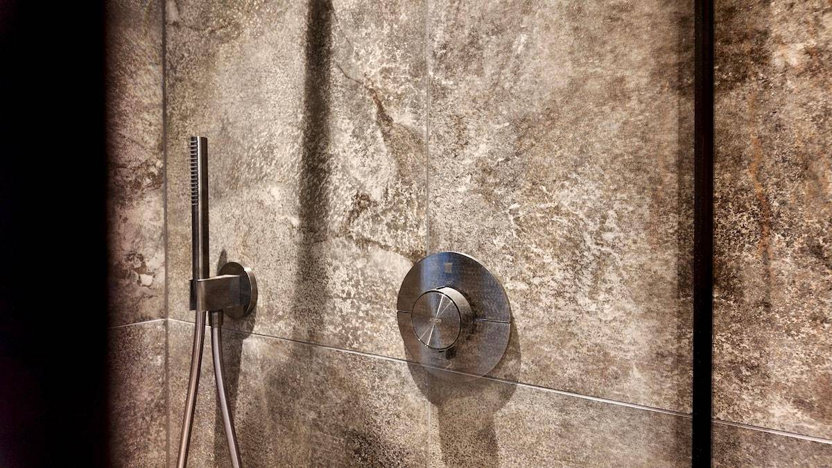 Detailansicht einer modernen Duscharmatur in einem Badezimmer mit strukturierten Fliesen.