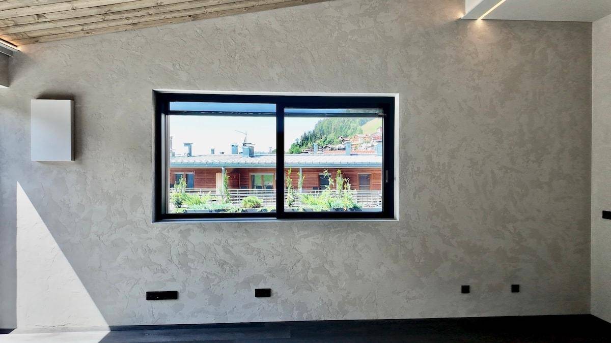 Heller Raum mit strukturierten Wänden, Holzboden und einem Fenster mit Blick auf die Umgebung.