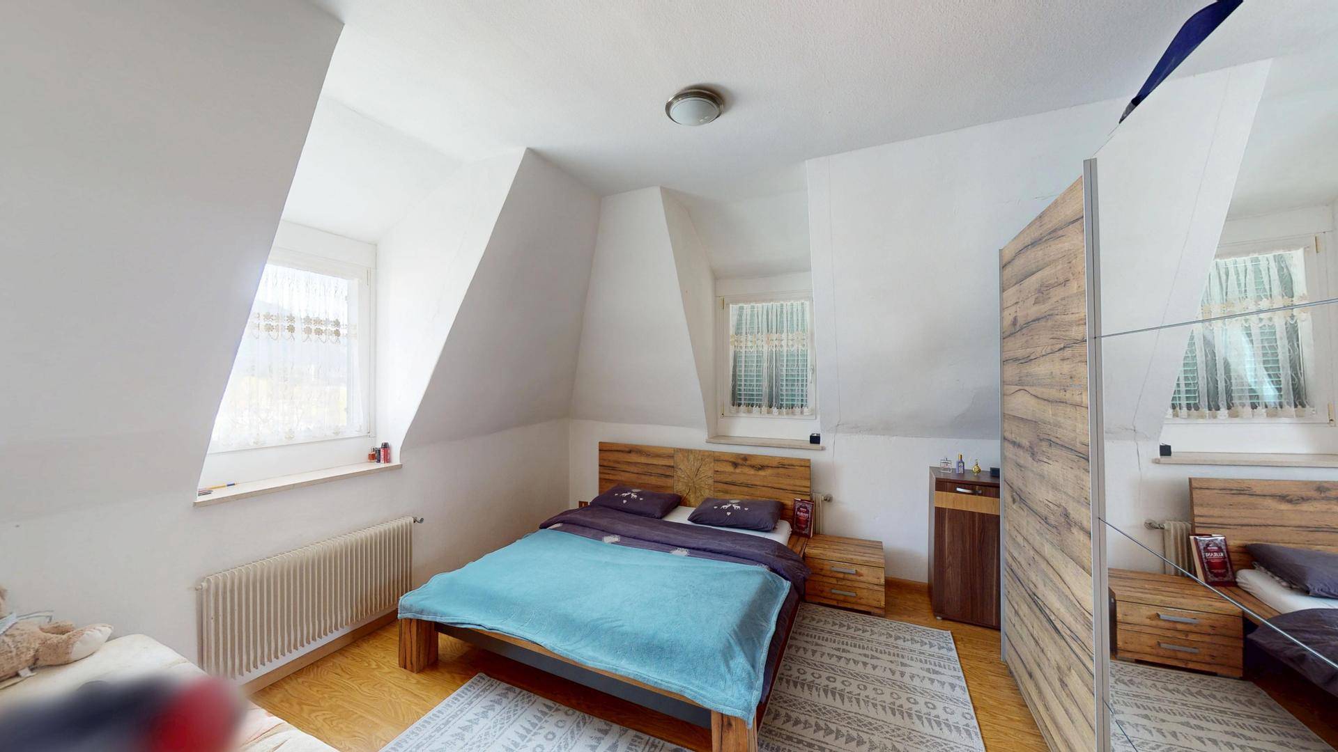 Schlafzimmer mit Dachschrägen, einem Holzbett, Nachttischen und einem großen Spiegelschrank.