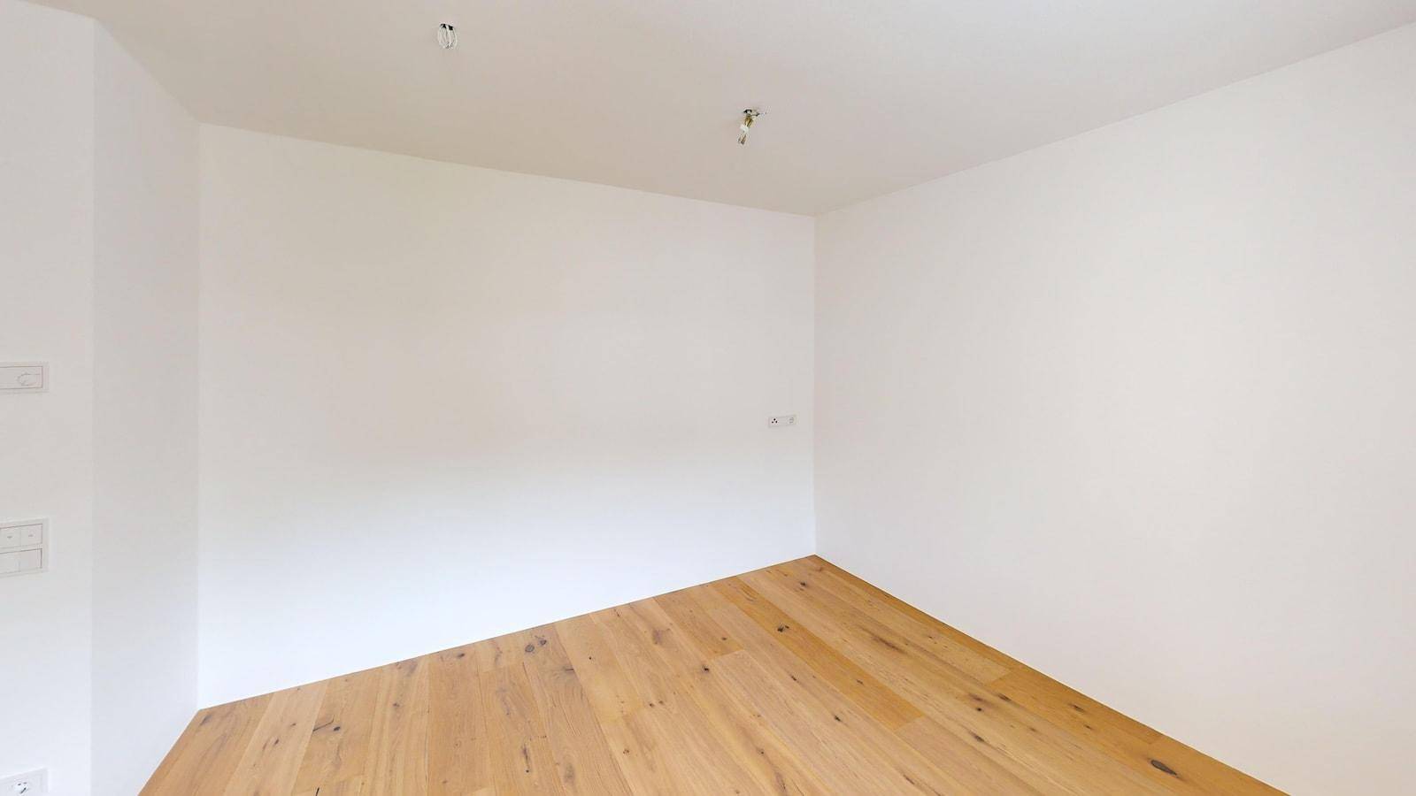 Leeres Zimmer mit hellem Parkettboden und weißen Wänden, bereit für individuelle Gestaltung.