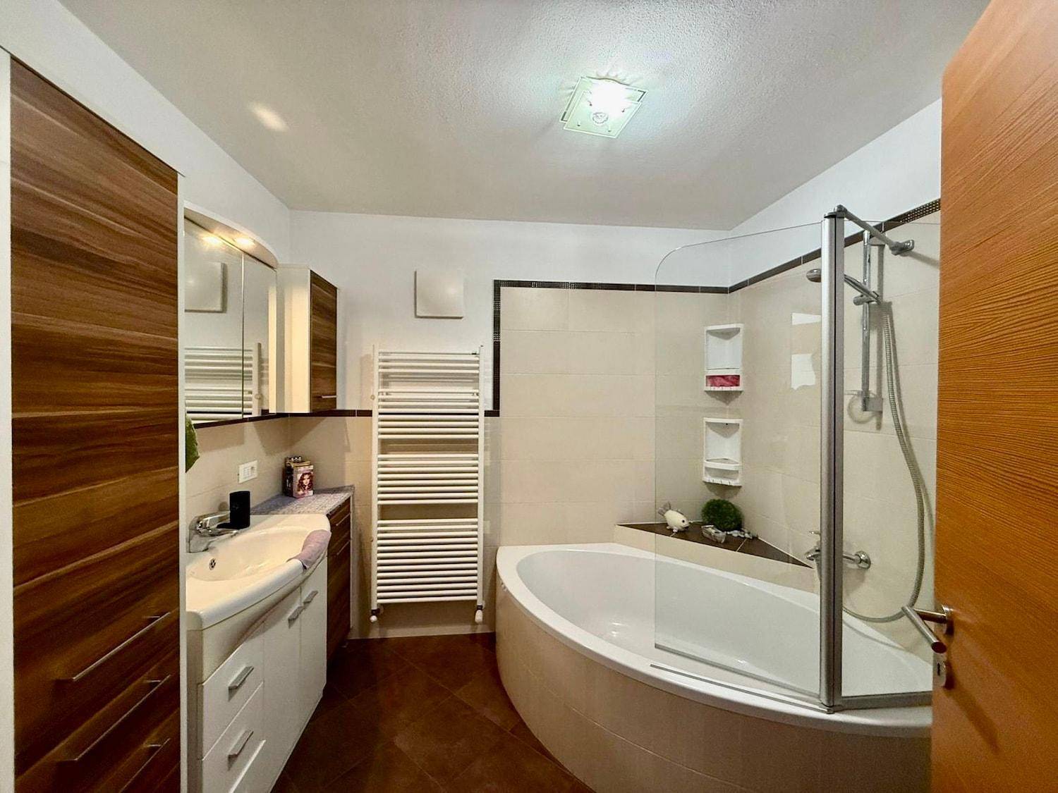 Modernes Badezimmer mit Eckbadewanne, Dusche, Einzelwaschbecken und beheiztem Handtuchhalter.