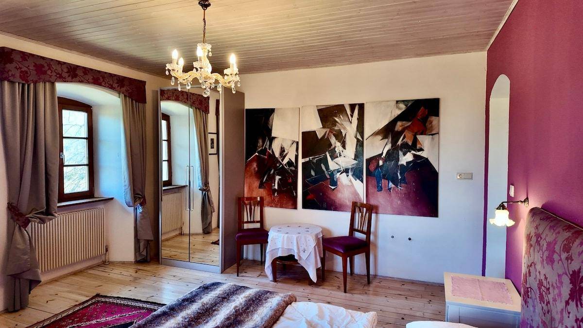 Schlafzimmer mit Holzboden, Kronleuchter, großem Spiegelschrank und abstrakten Kunstwerken an der Wand.