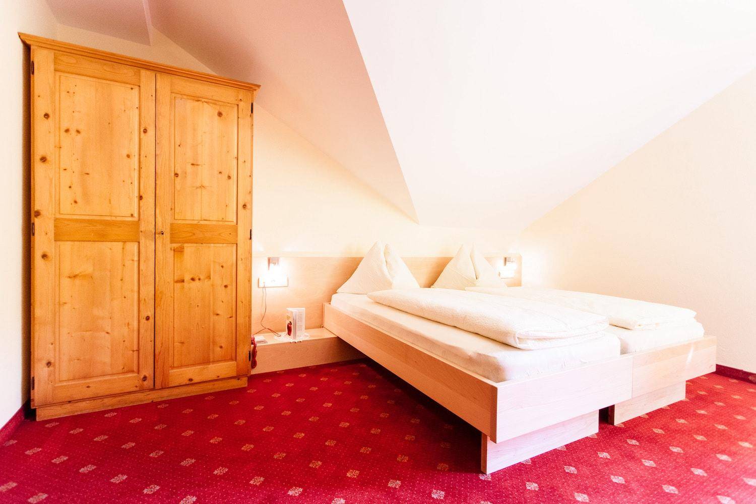 Schlafzimmer mit rotem Teppichboden, Holzschrank und zwei Einzelbetten unter Dachschräge.
