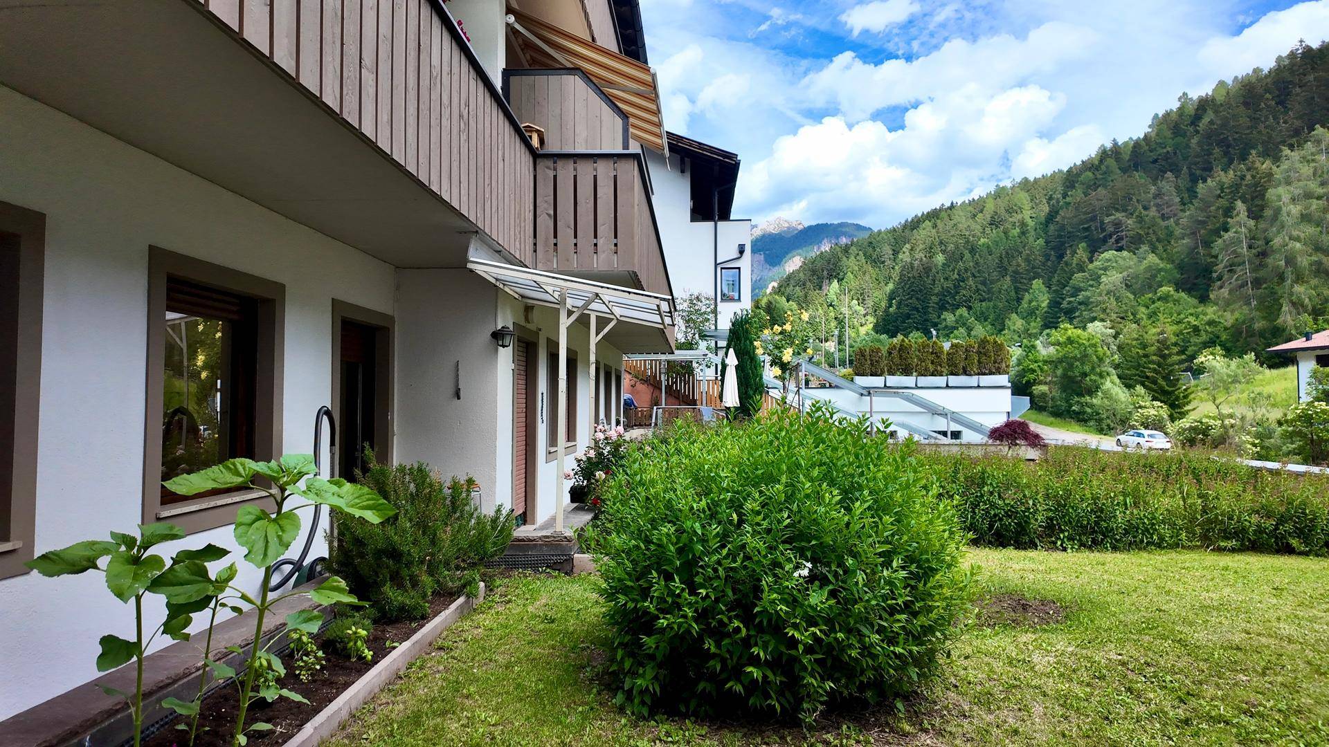 Gebäudefassade mit Gartenbereich und einem weiten Blick auf die umliegende Berglandschaft.