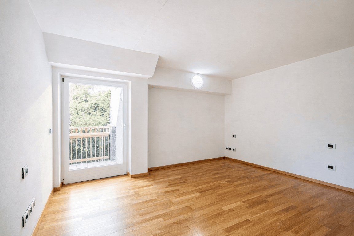 Leeres Schlafzimmer mit Holzboden, Fenster und Balkonzugang.