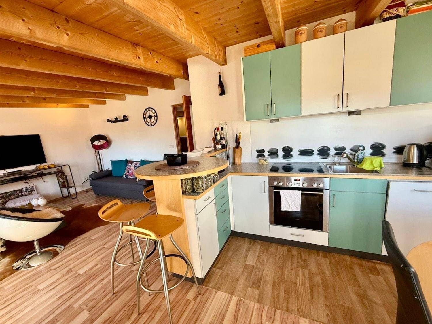 Offene Küche mit mintgrünen und weißen Schränken, Holzbalkendecke und Essbereich.