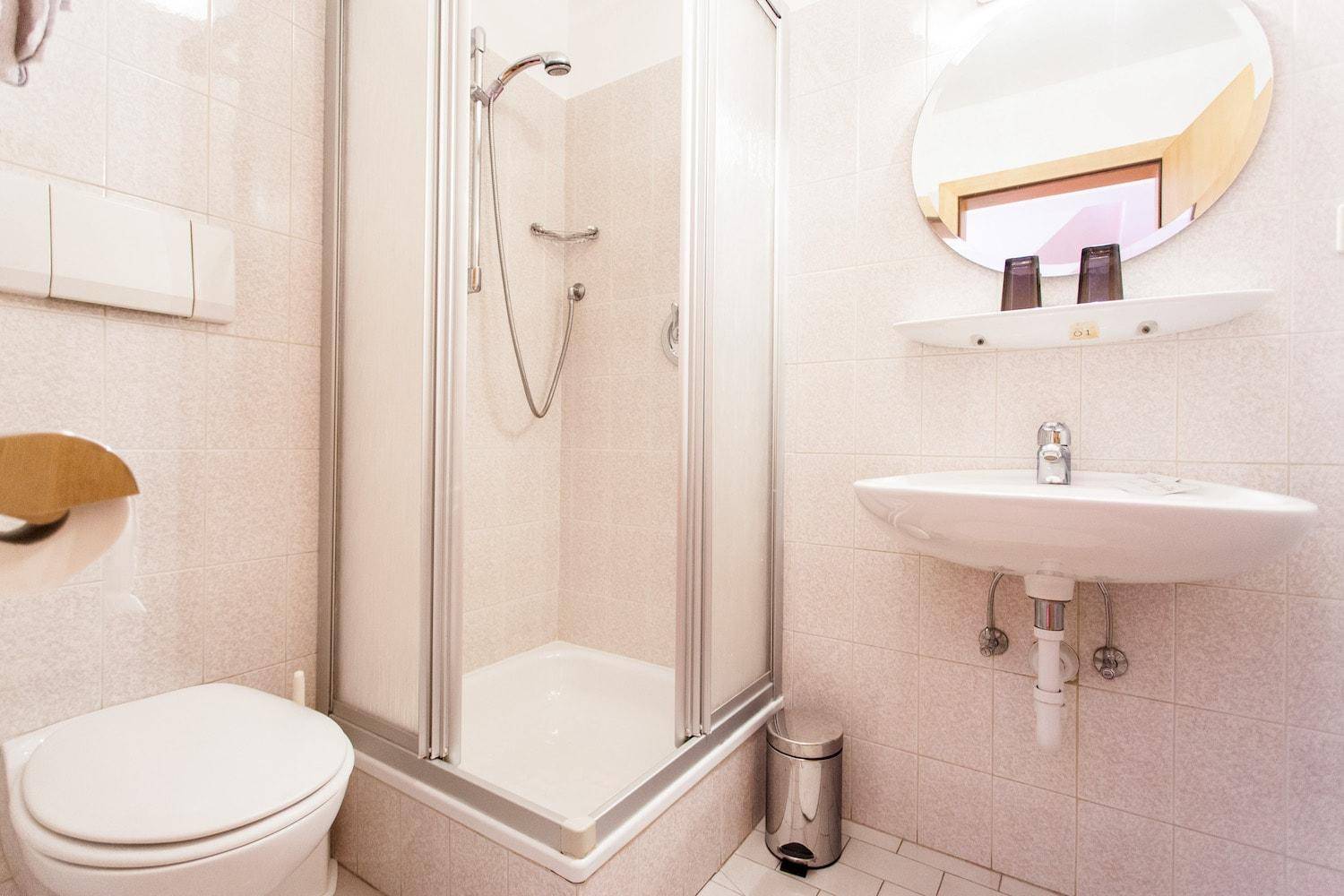Funktionales Badezimmer mit Duschkabine, WC und Waschbecken in hellen Fliesen.