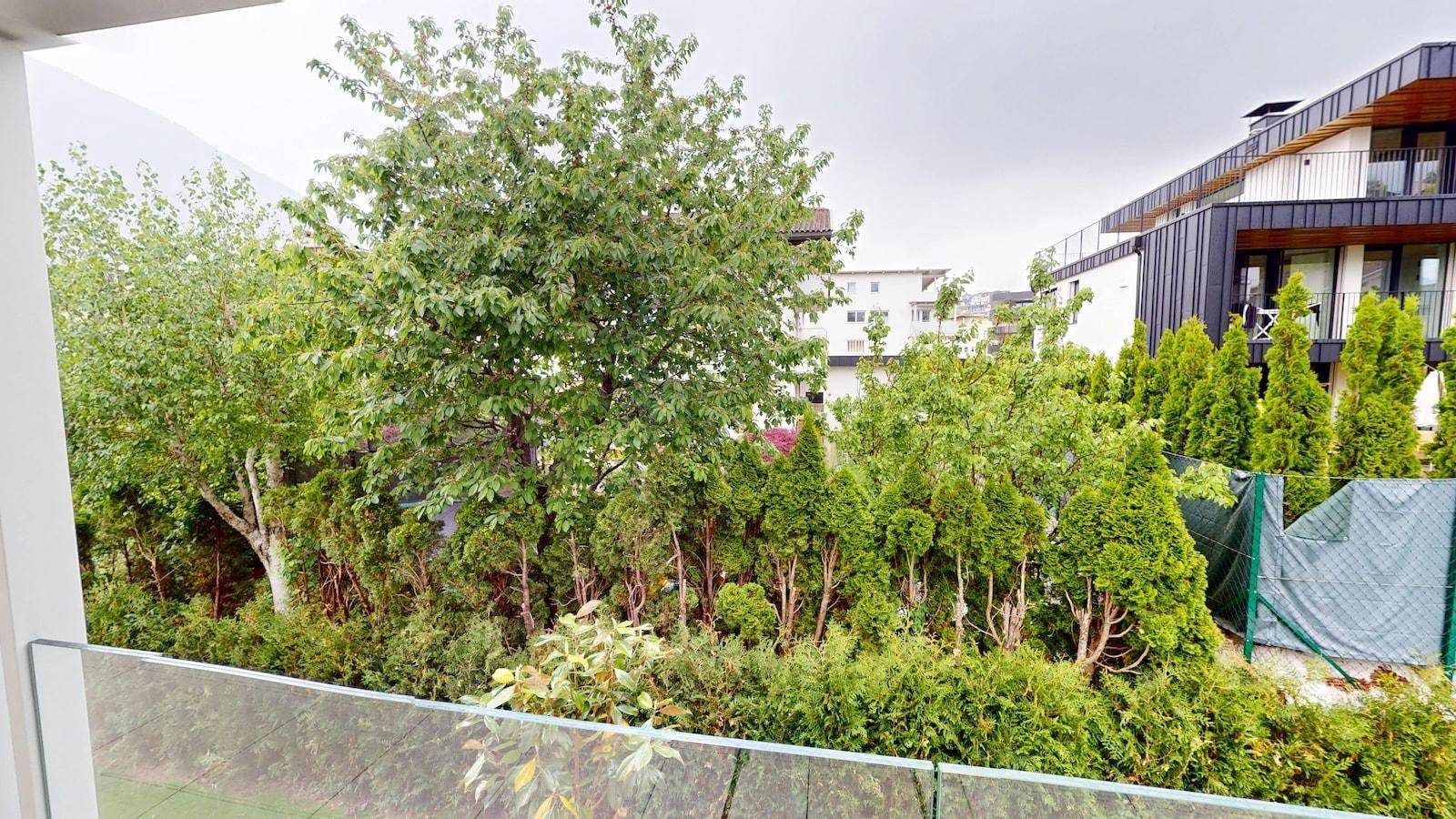 Blick vom Balkon auf einen gepflegten Gartenbereich mit Bäumen und Hecken.