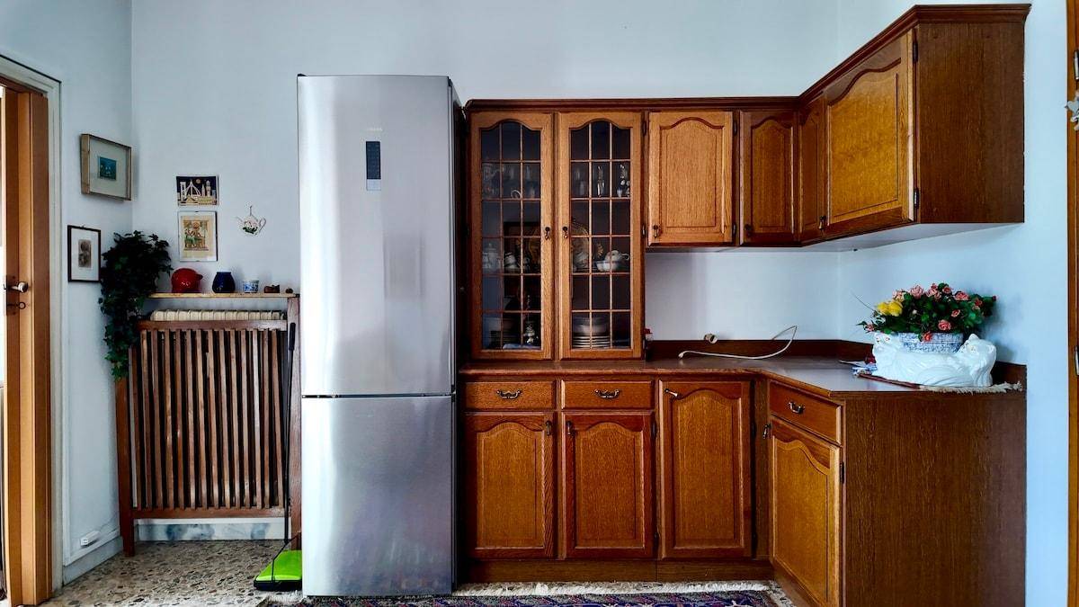 Funktionale Küche mit Holzschränken, großem Kühlschrank und Heizkörper unter dem Fenster.