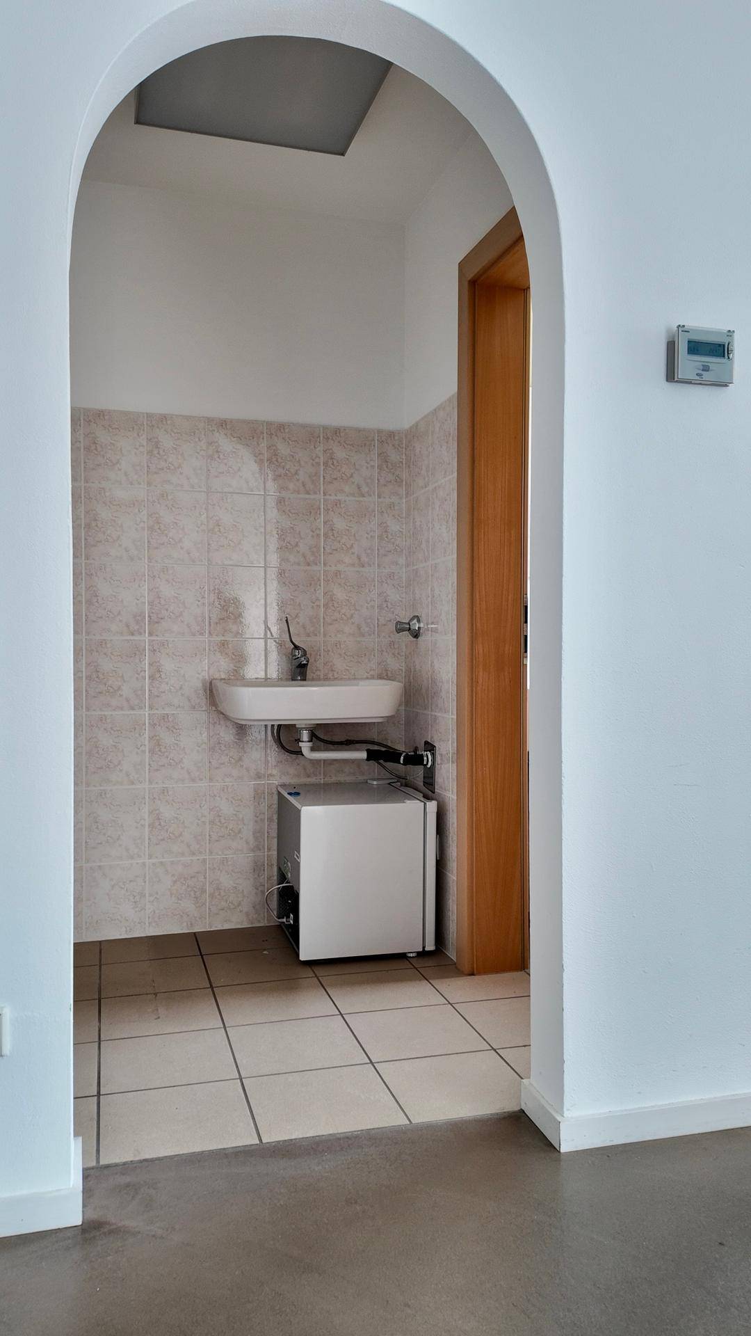 Kleiner Sanitärbereich mit Waschbecken und Fliesen an Wänden und Boden, zugänglich durch einen Bogen.