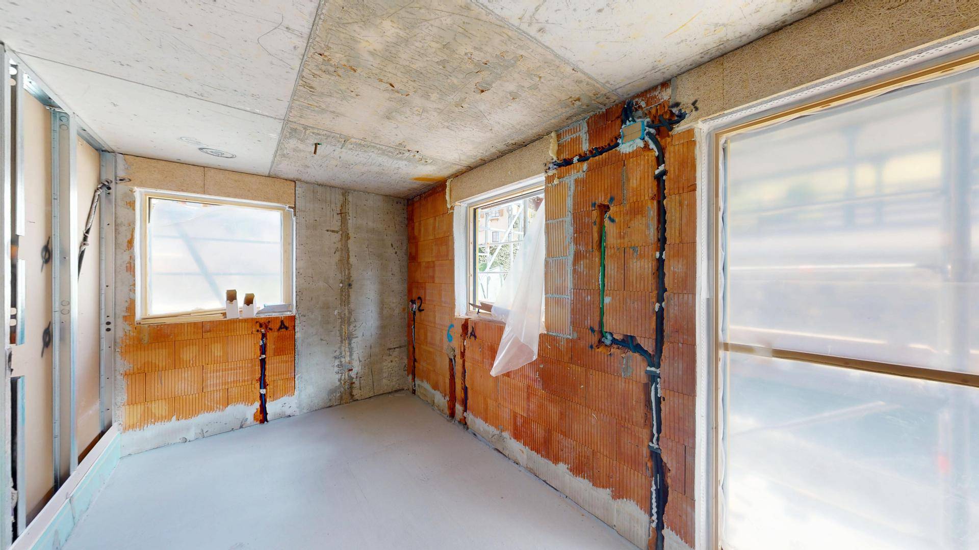 Innenraum im Rohbau mit sichtbaren Ziegeln und vorbereiteten Anschlüssen für Sanitär.