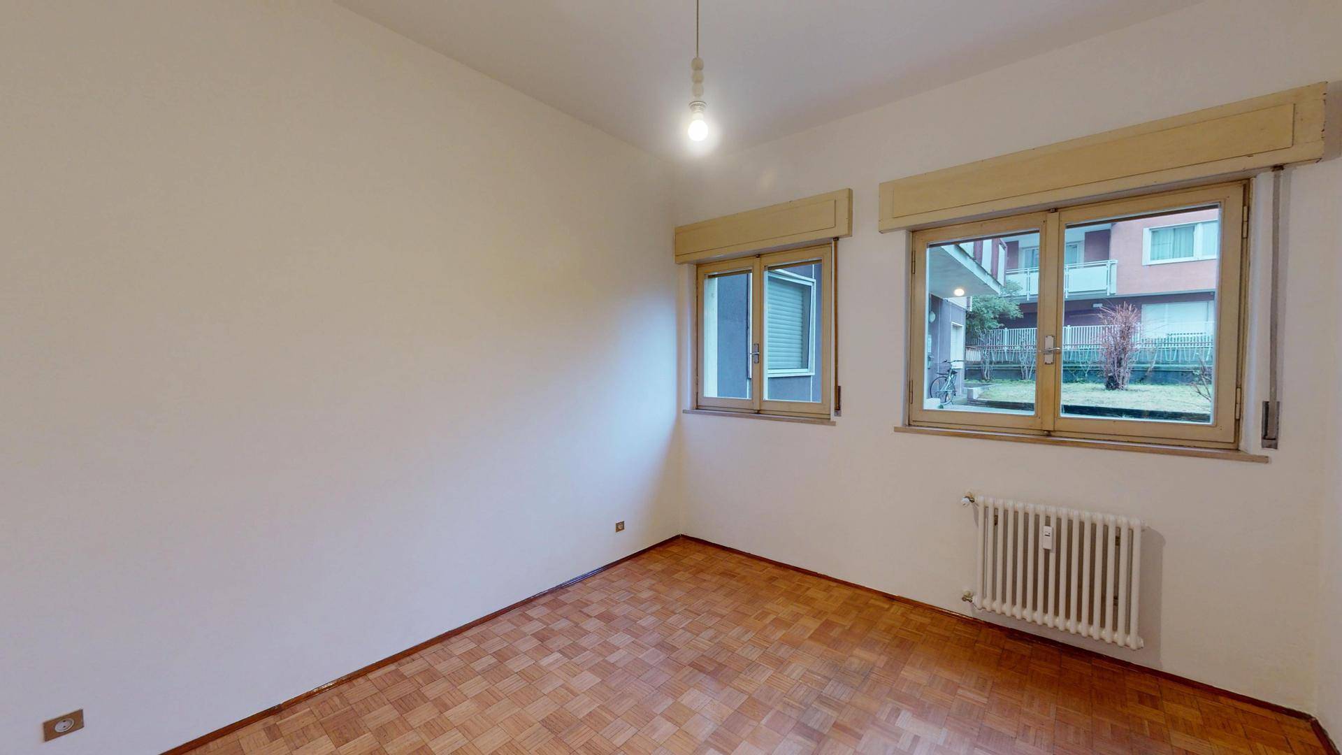 Geräumiges Zimmer mit Parkettboden und Blick ins Grüne durch große Fenster.