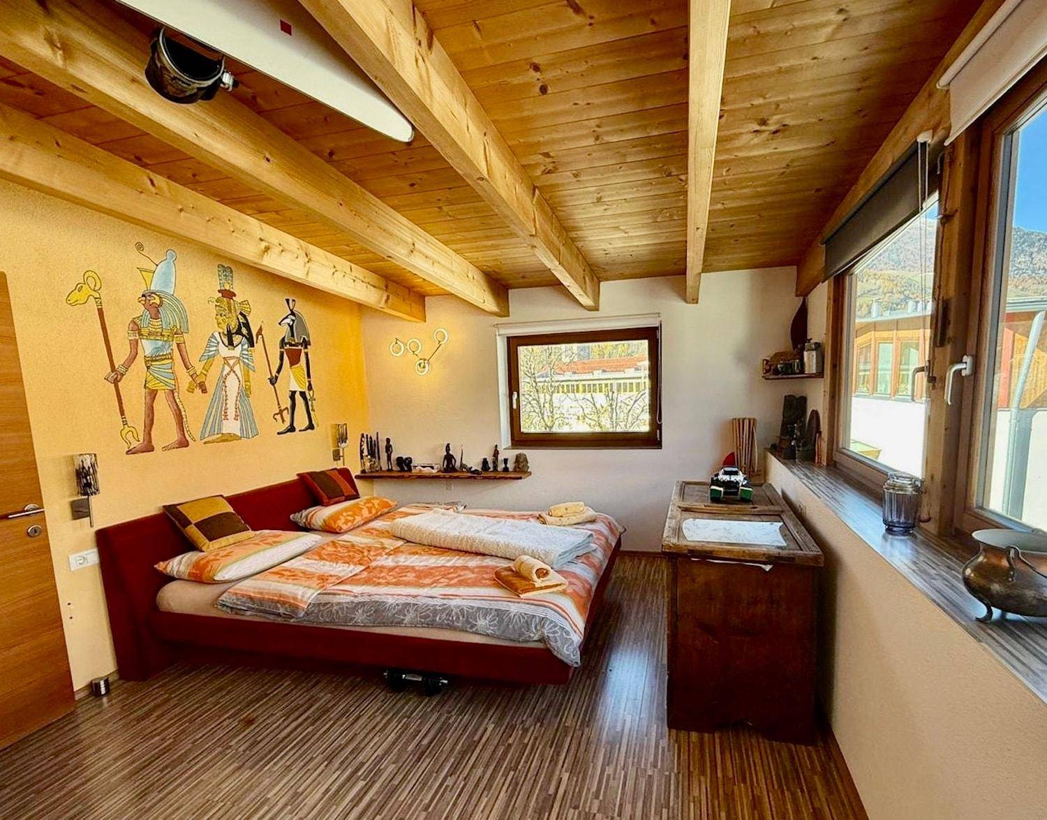 Schlafzimmer mit Holzbalkendecke, Parkettboden und ägyptisch inspirierten Wandmalereien.