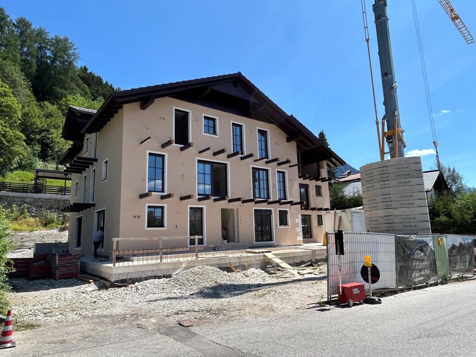 Seitenansicht des Neubaus mit beiger Fassade und dunklem Dach, umgeben von Baustelle und Kran.