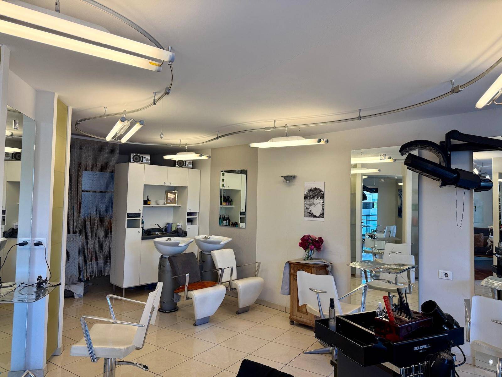 Geräumiger Friseursalon mit mehreren Bedienplätzen, Waschbecken und heller Beleuchtung.