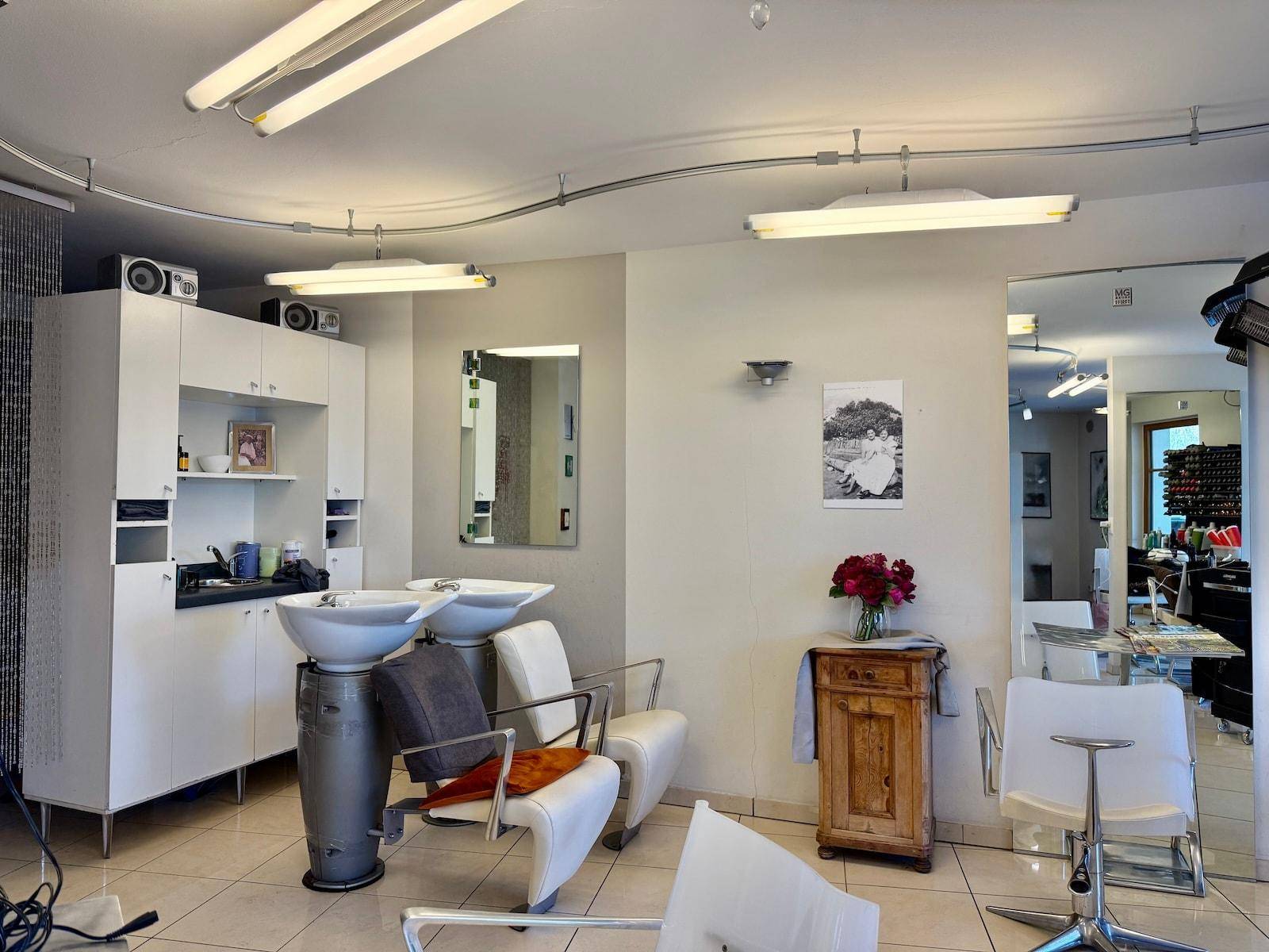 Bereich mit Waschbecken und Stühlen im Friseursalon, ergänzt durch einen kleinen Schrank.
