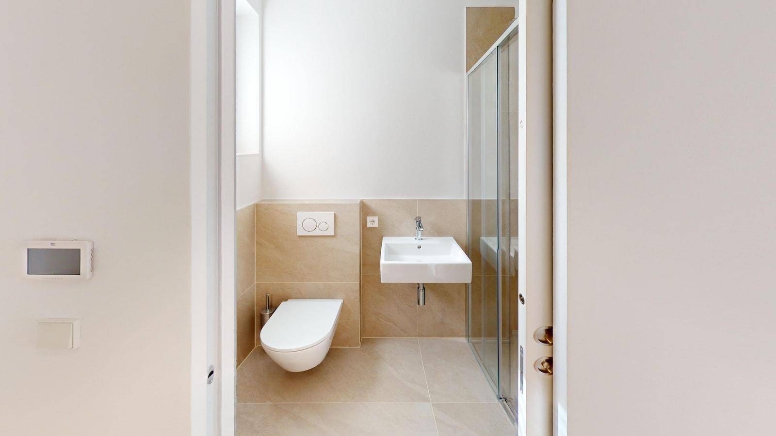 Kleines Badezimmer mit WC, Waschbecken und Duschkabine, komplett gefliest.