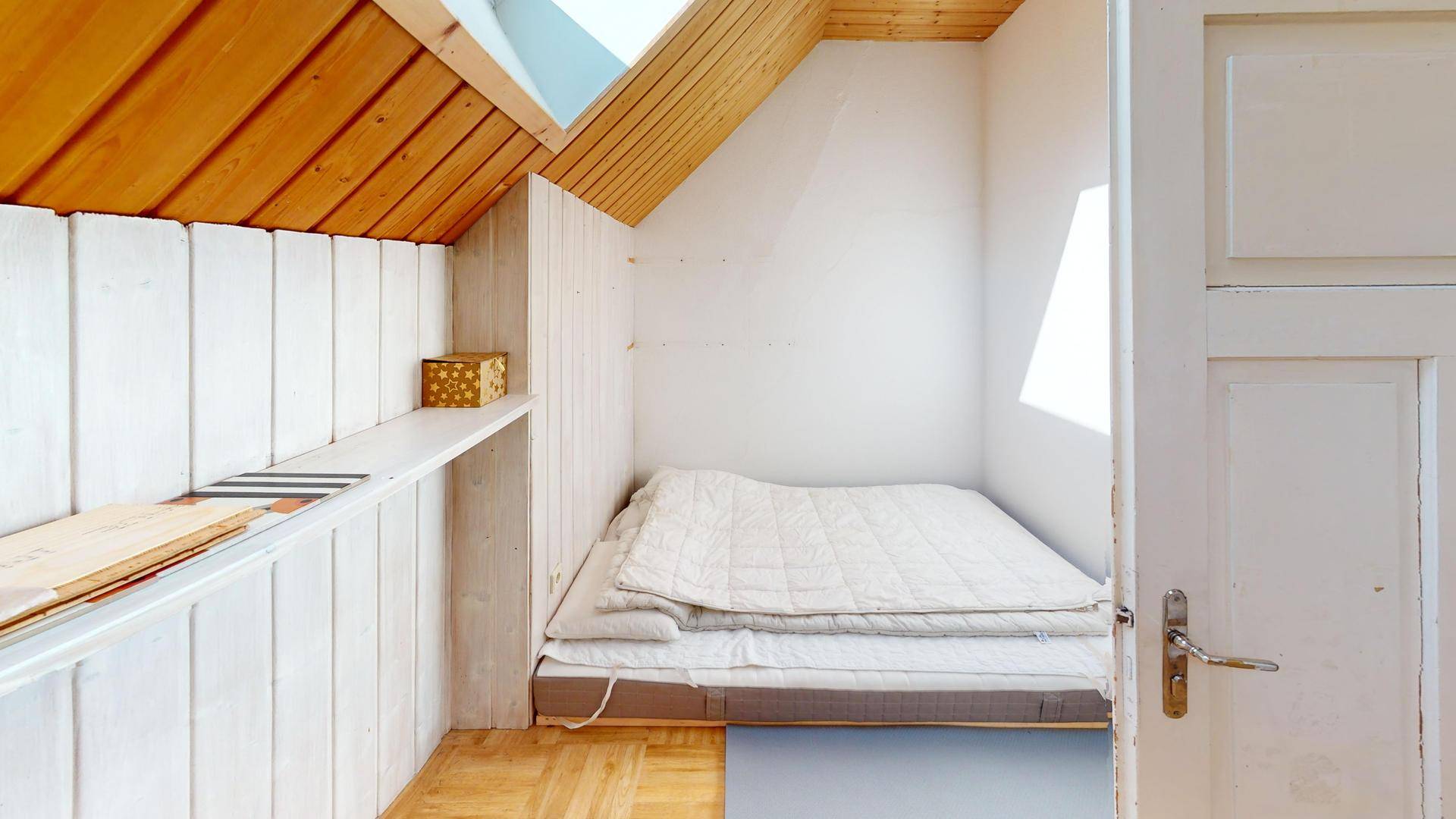 Kleiner Schlafbereich mit Holzdielenboden, Dachschräge und Holzverkleidung.