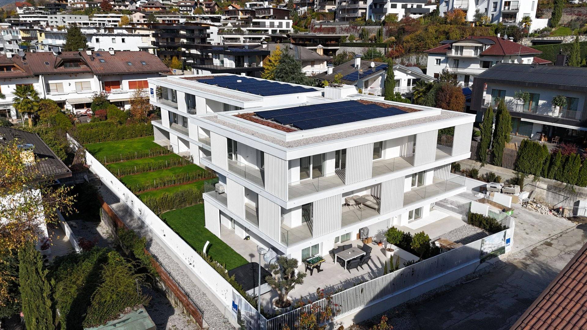 Luftaufnahme des modernen Wohngebäudes mit Terrassen, Gärten und Photovoltaikanlage auf dem Dach.
