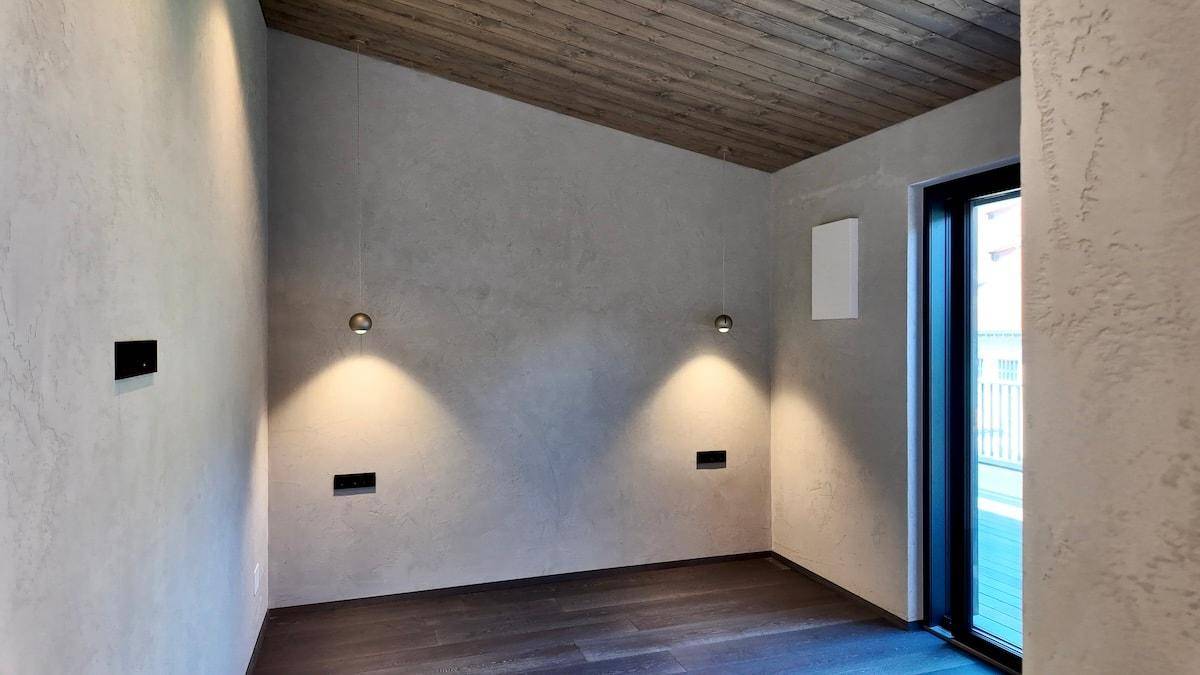Heller Raum mit strukturierten Wänden, Holzboden und Zugang zu einem Außenbereich.
