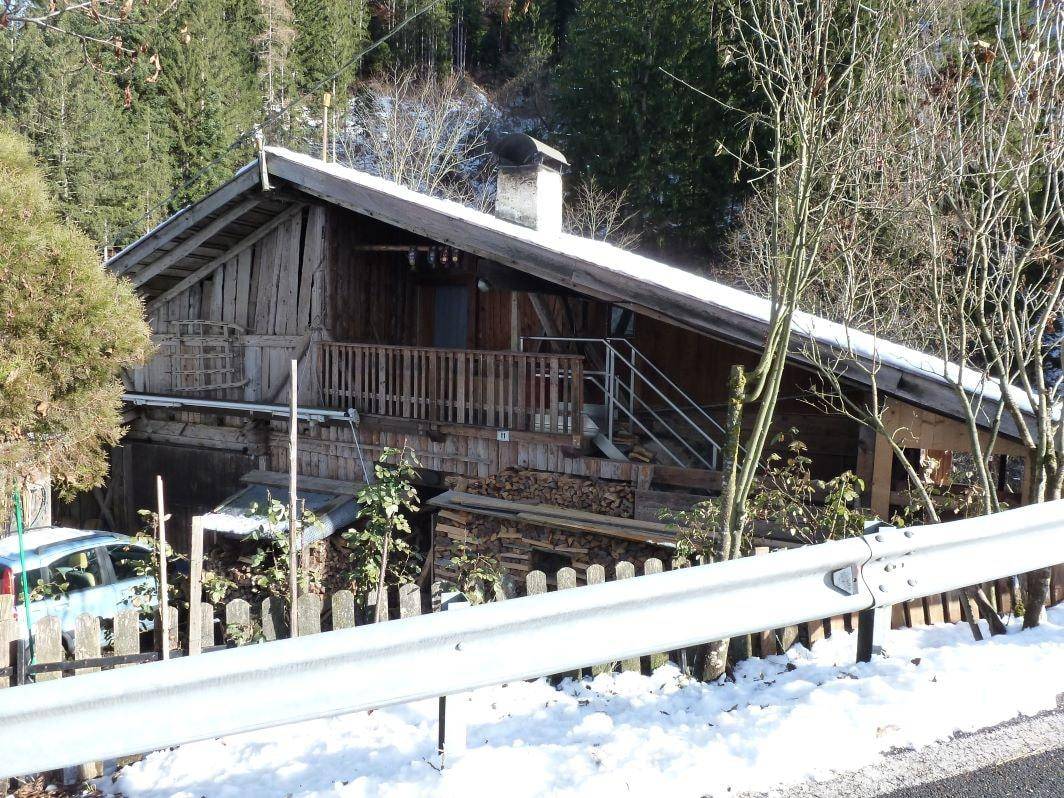 Traditionelles Holzchalet in winterlicher Umgebung, umgeben von Wald und Schnee, mit einer Straße im Vordergrund.