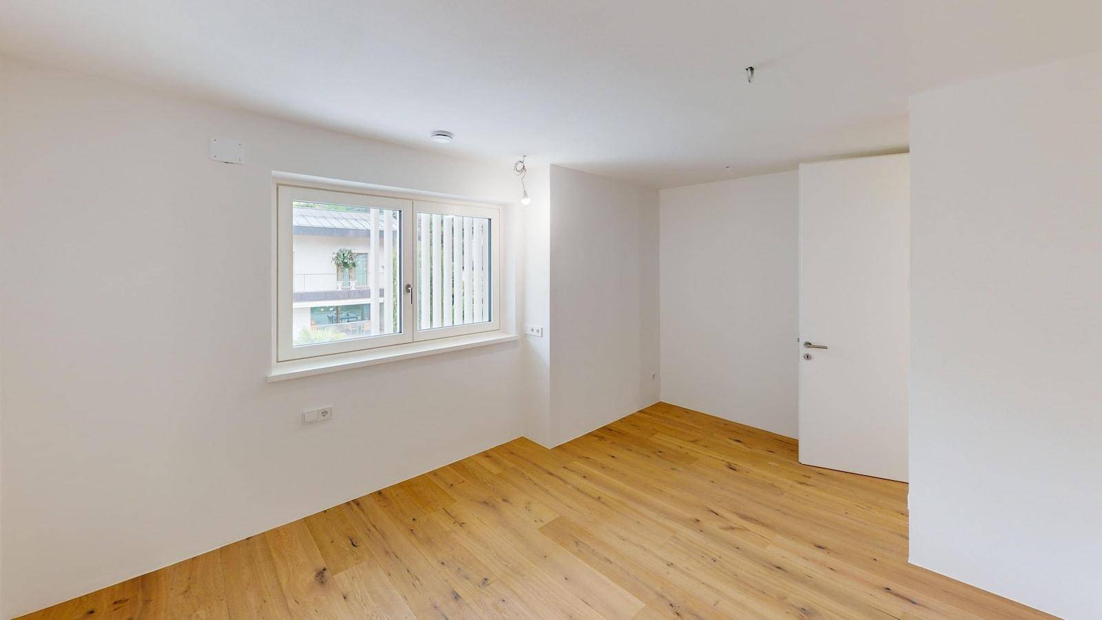 Geräumiges Schlafzimmer mit Parkettboden und einem großen Fenster, das eine angenehme Atmosphäre schafft.
