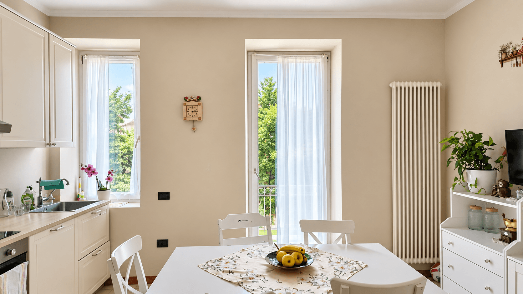 Essbereich in der Küche mit weißem Tisch, Stühlen und Blick ins Grüne durch die Fenster.
