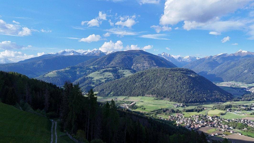 Panoramablick über ein weites Tal mit verstreuten Dörfern, umrahmt von bewaldeten Bergen und blauem Himmel.