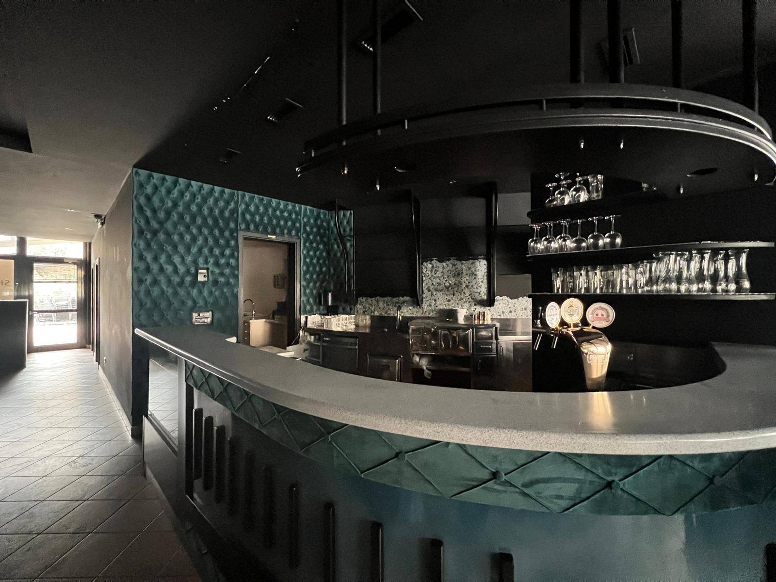Dunkle Bar mit Theke, Gläserregalen und Zapfanlage in einem stilvollen Ambiente, bereit für Gäste.