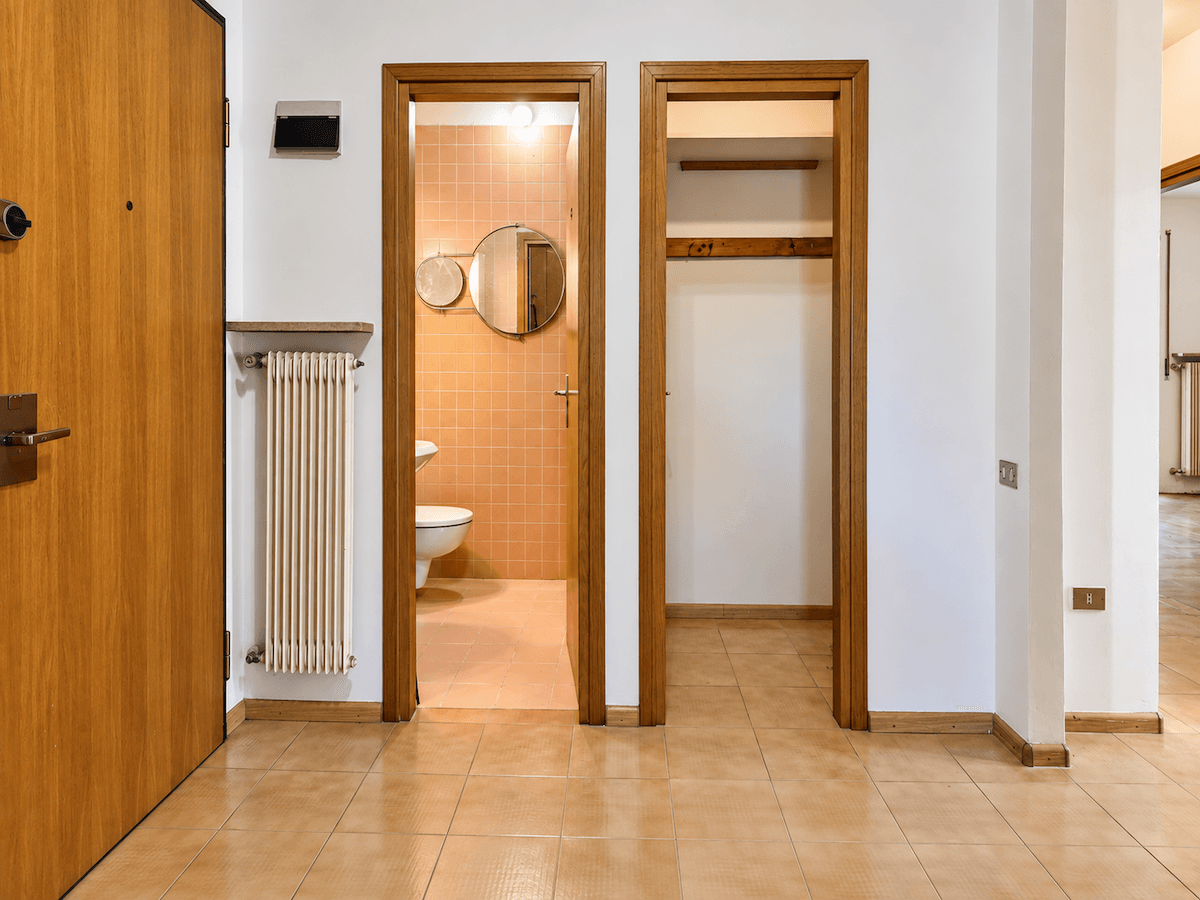 Flur mit Fliesenboden, Heizkörper und Zugang zu einem Badezimmer und einem Abstellraum.