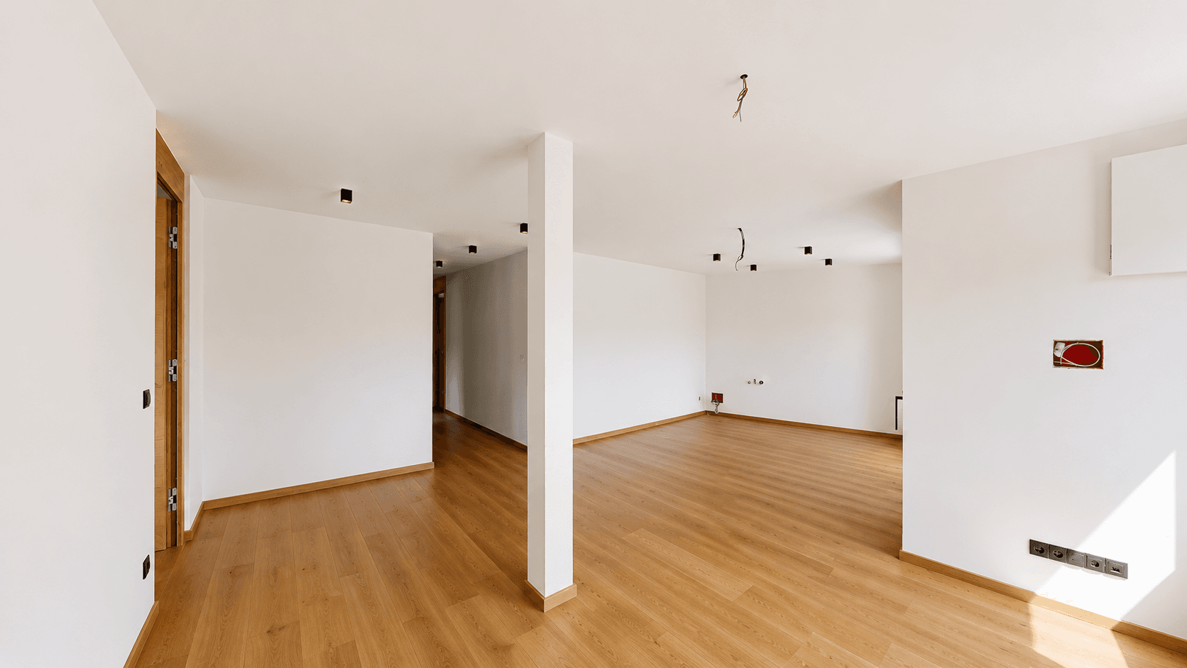 Geräumiger, heller Raum mit Holzboden und weißen Wänden, ideal für einen Wohnbereich.