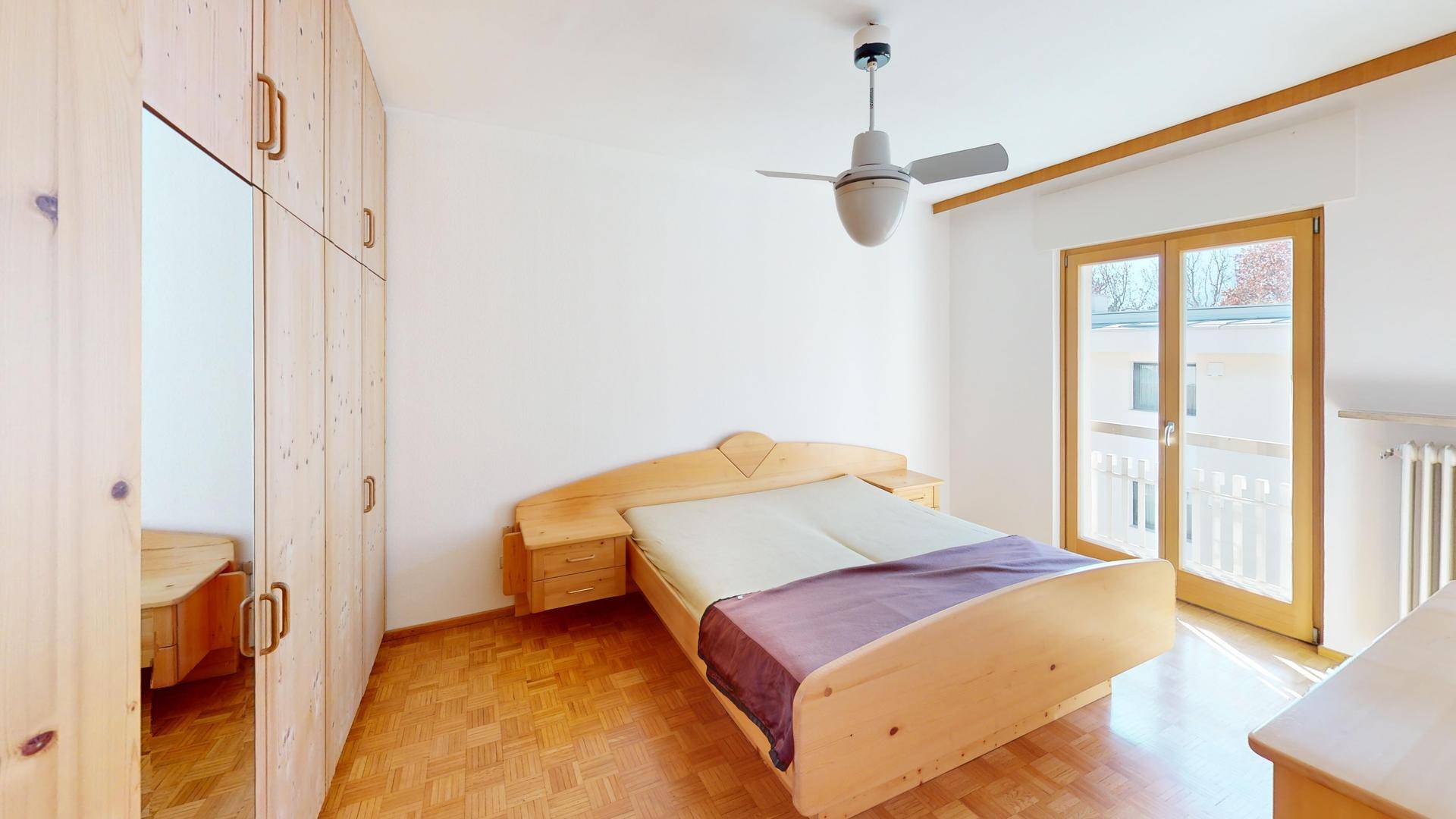 Helles Schlafzimmer mit Holzbett, Einbauschränken und Zugang zu einem französischen Balkon.