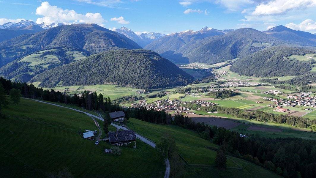 Luftaufnahme eines ländlichen Anwesens mit traditionellen Gebäuden in einer grünen Hügellandschaft.