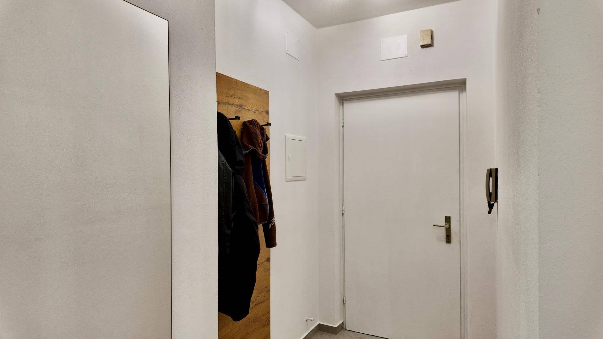 Heller Flur mit weißer Tür, Gegensprechanlage und einer Garderobe in Holzoptik.