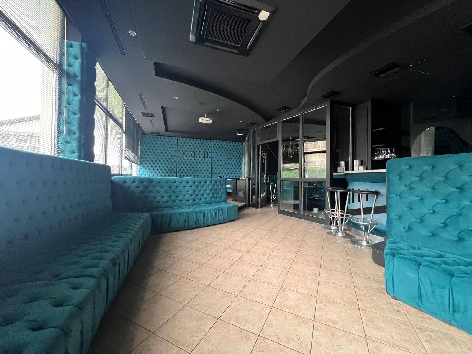 Geräumiger Lounge-Bereich mit türkisfarbenen Sitzgelegenheiten, dunkler Decke und großen Fenstern, die viel Tageslicht hereinlassen.