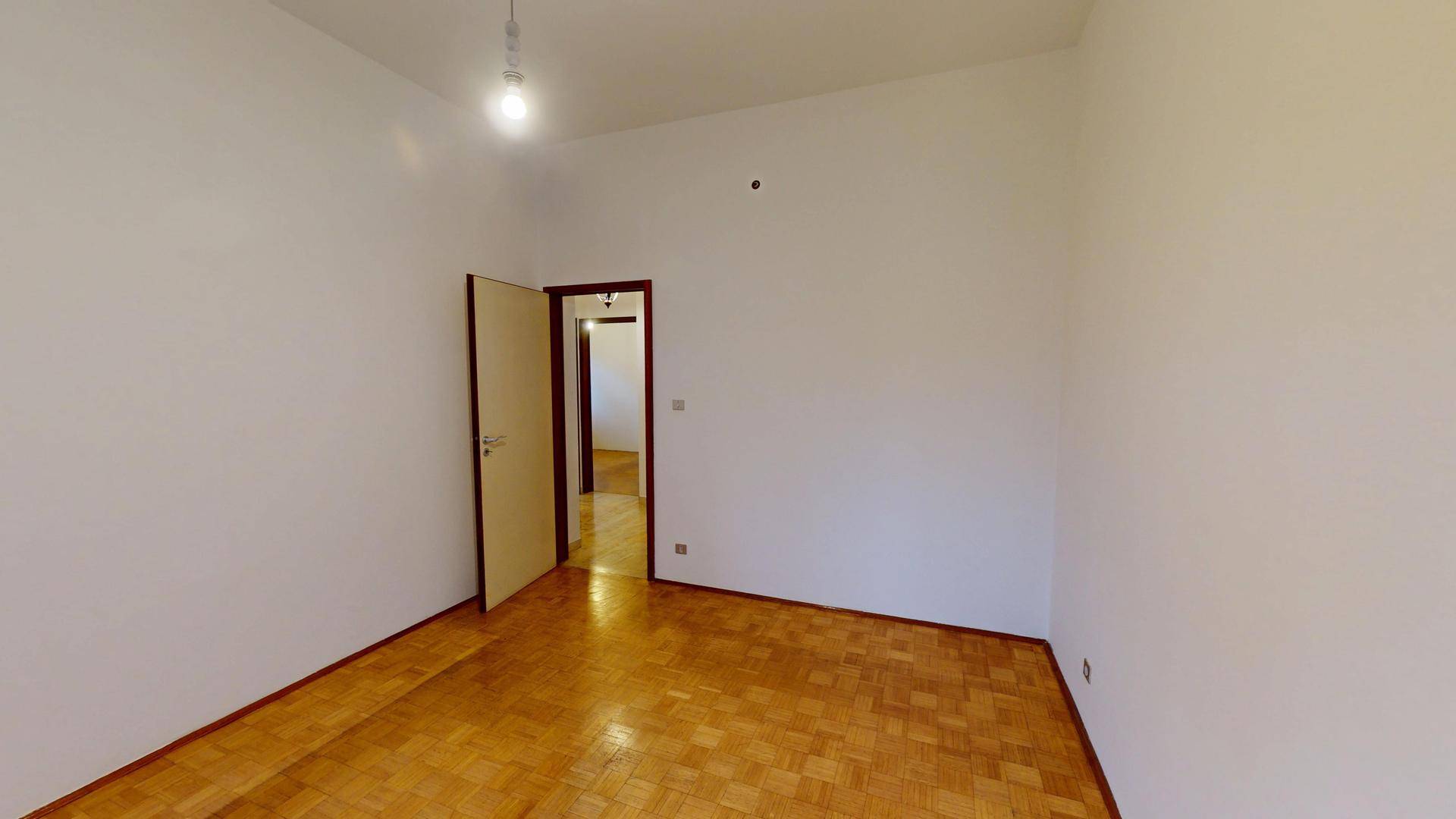 Geräumiges Zimmer mit Parkettboden und einer Tür, die den Zugang zu weiteren Räumen ermöglicht.