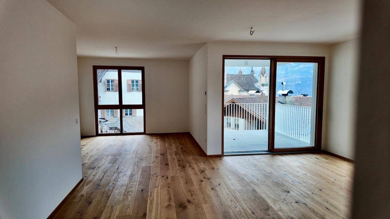 Heller Wohnraum mit Holzboden, großen Fenstern und Zugang zu einem Balkon mit Aussicht.