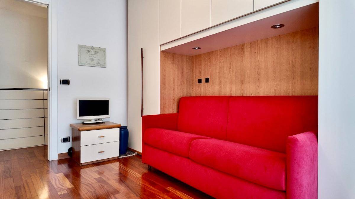 Gemütlicher Wohnbereich mit rotem Sofa, Holzboden und Einbauschränken.
