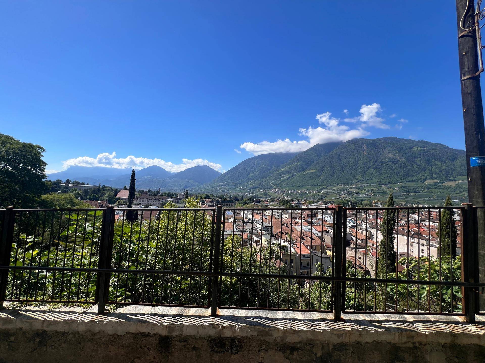 Panoramablick auf eine Stadt im Tal, umgeben von majestätischen Bergen unter strahlend blauem Himmel.