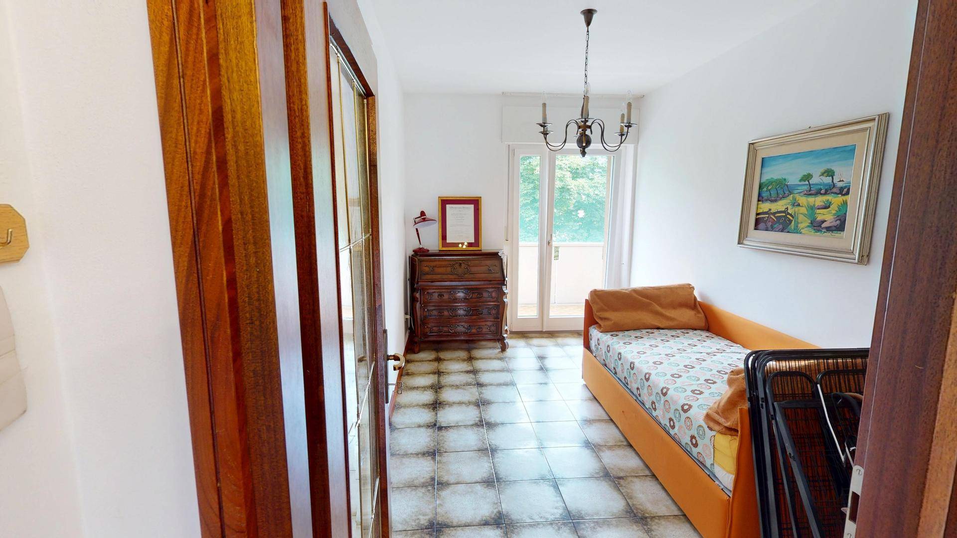 Schlafzimmer mit Einzelbett, Fliesenboden und Zugang zu einem kleinen Balkon mit Ausblick.