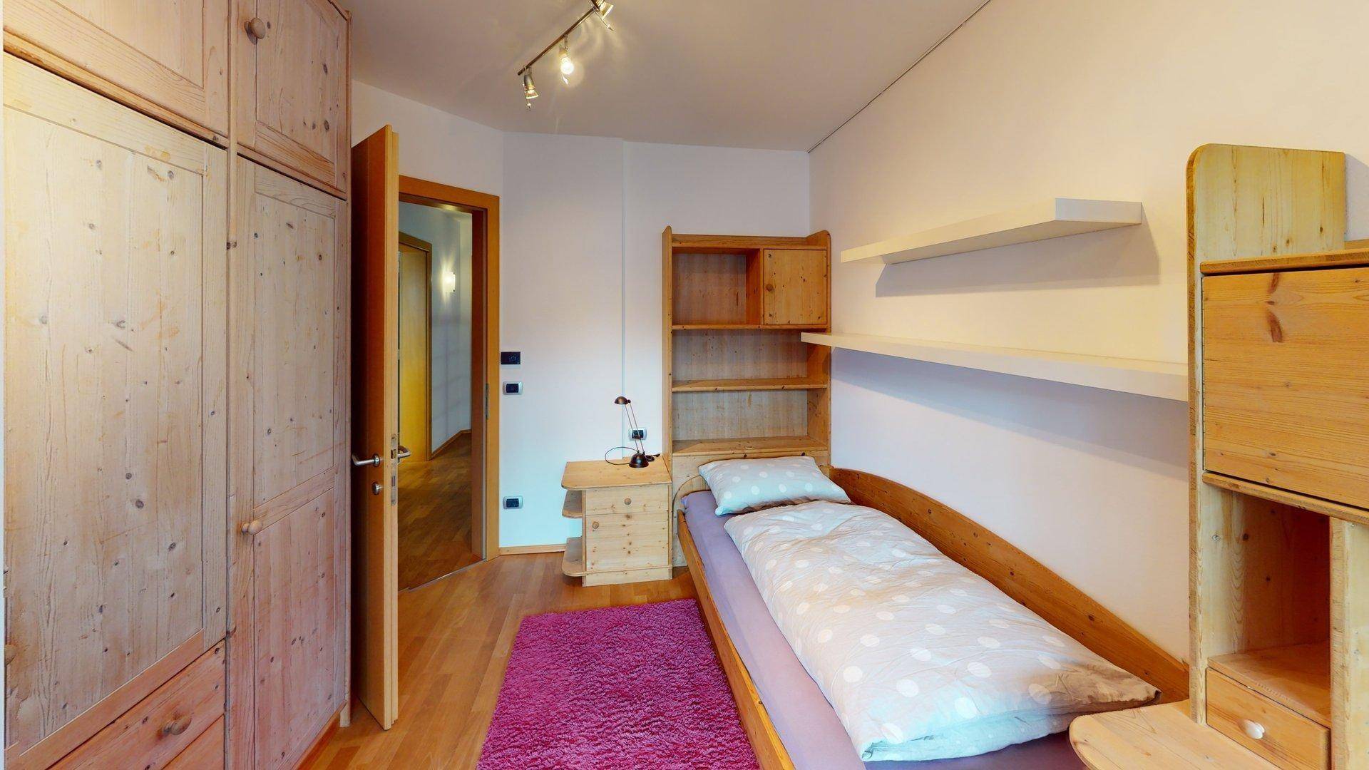 Helles Schlafzimmer mit Einzelbett, Holzmöbeln und einem großen Kleiderschrank.