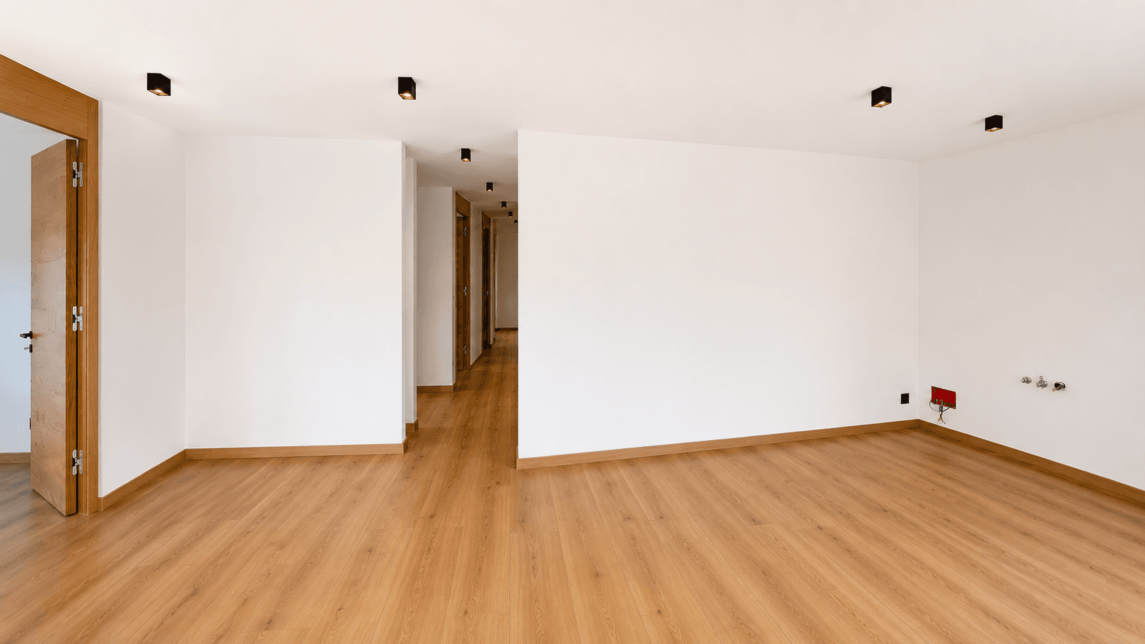 Heller Raum mit Holzboden und Blick in einen langen Flur mit mehreren Türen.